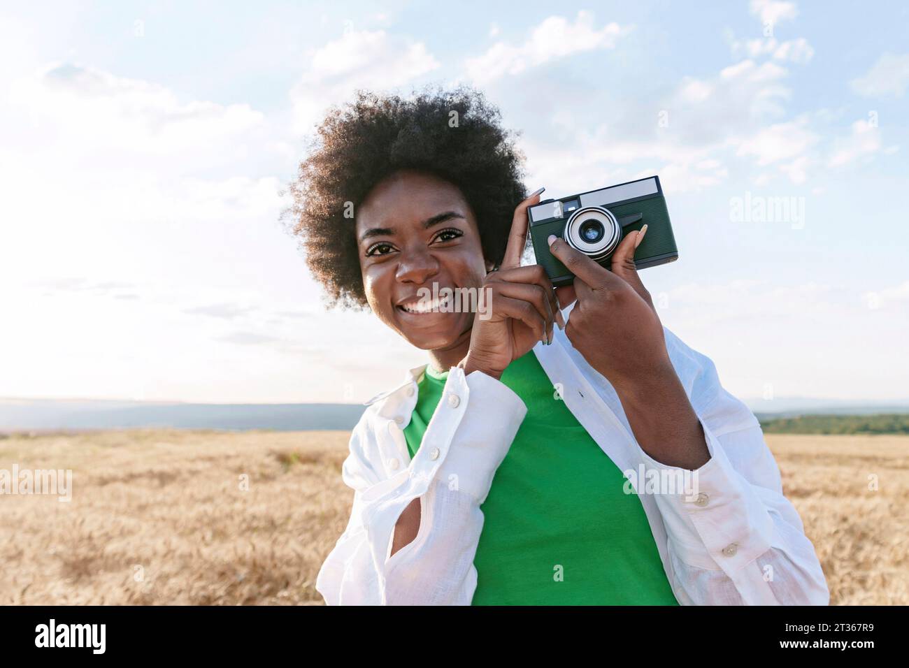 Smiling young woman holding camera in field Stock Photo