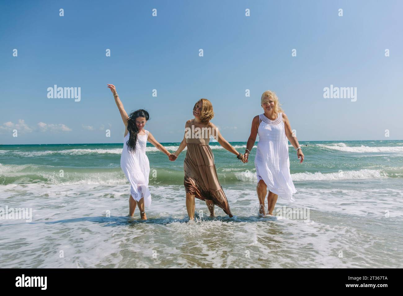 Women holding hands and walking together in sea at beach Stock Photo ...