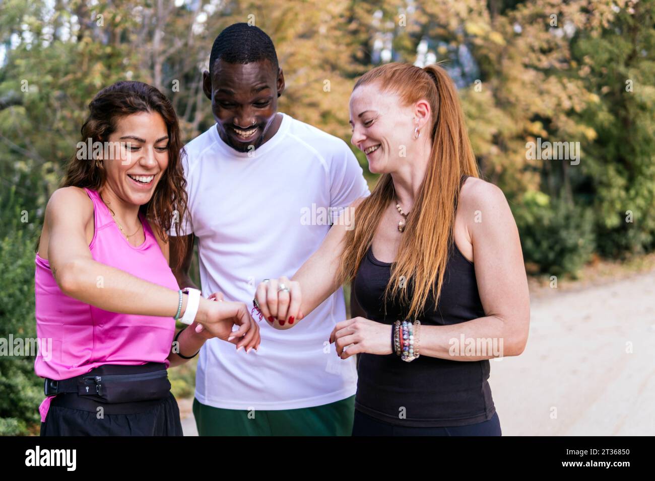 Happy friends using smart watch standing at park Stock Photo