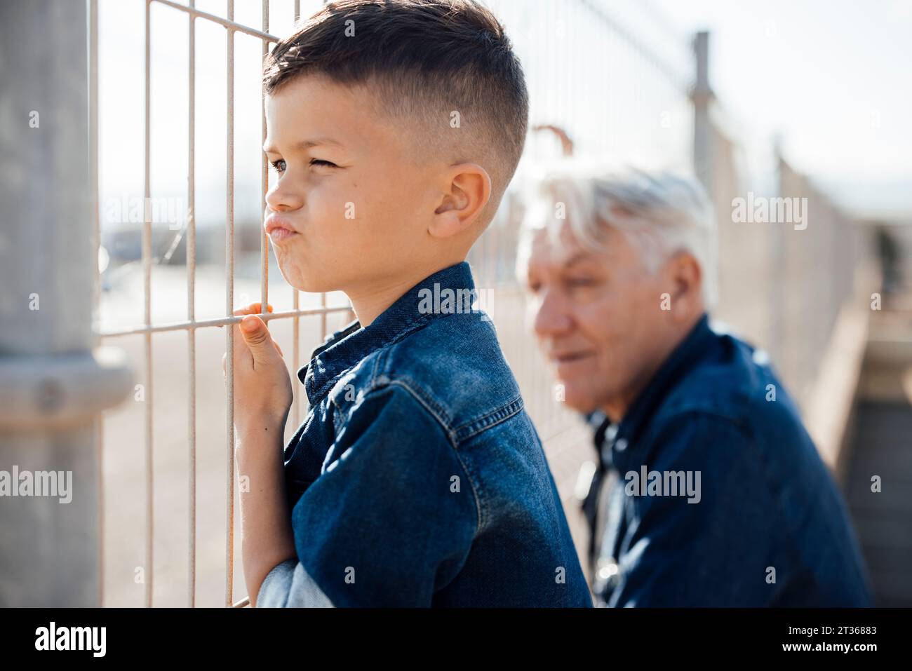 Curious boy puckering and looking through fence by grandfather Stock Photo