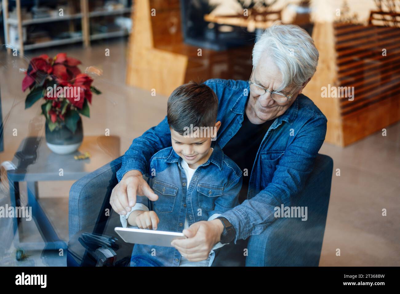 Boy using tablet PC sitting with grandfather at home Stock Photo