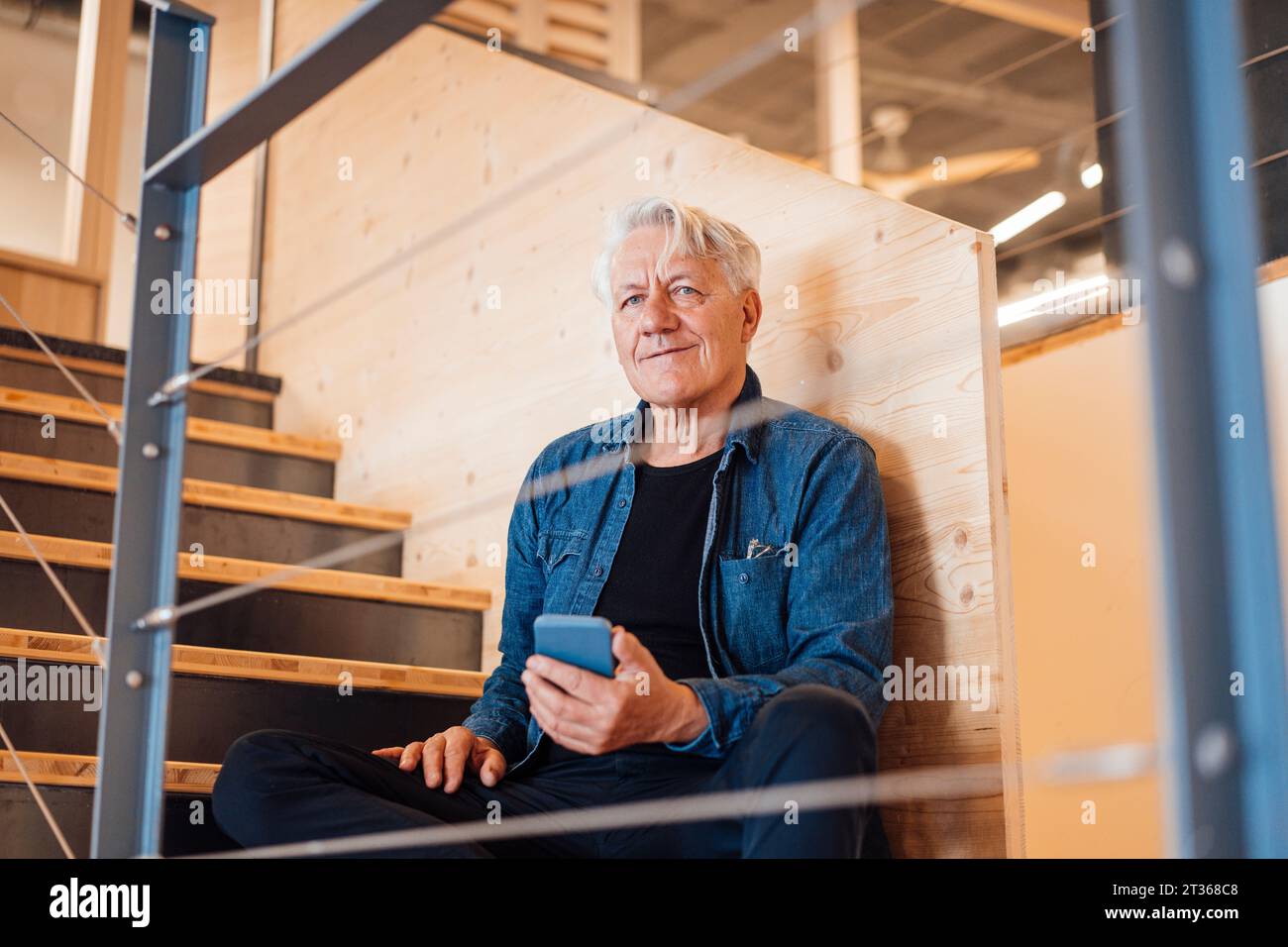 Thoughtful senior man holding smart phone at home Stock Photo