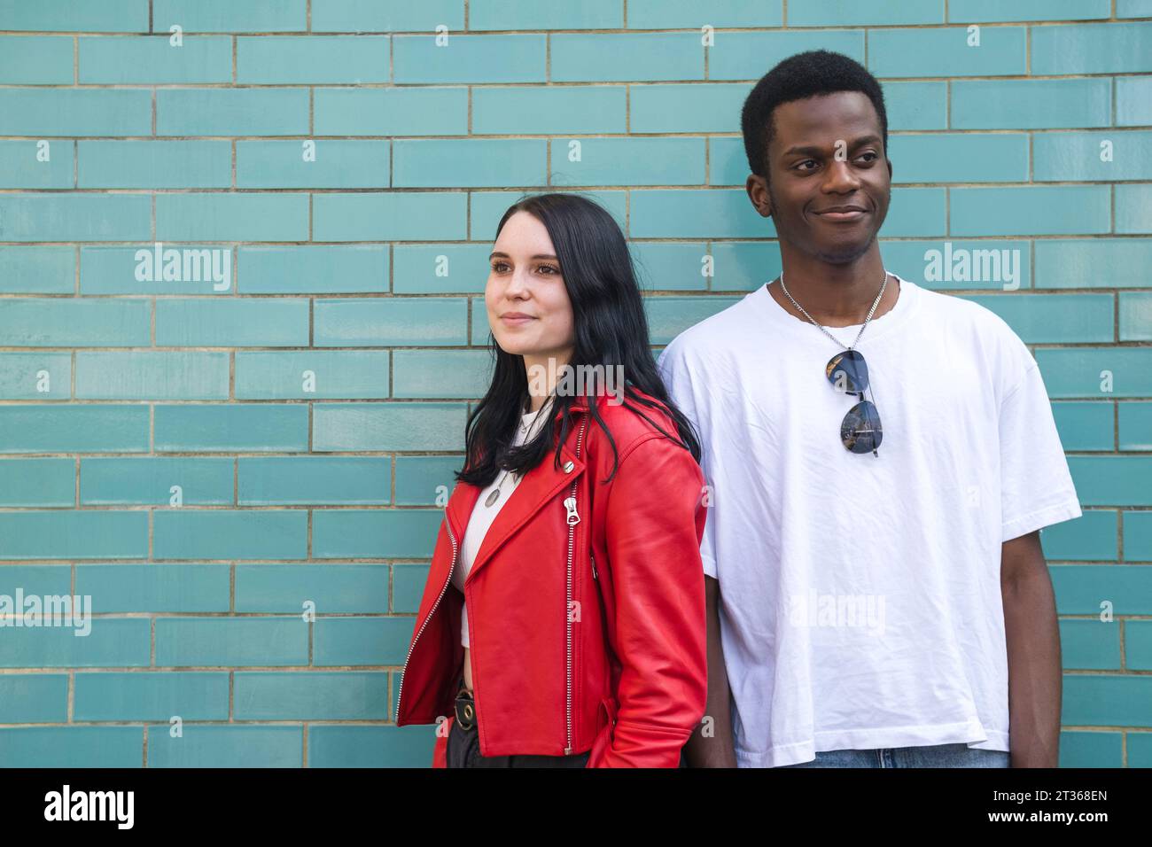 Smiling young woman standing with man in front of brick wall Stock Photo