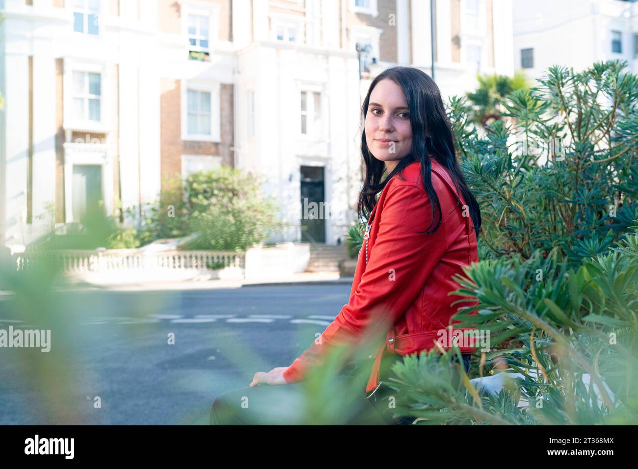 Smiling young woman sitting near plants Stock Photo