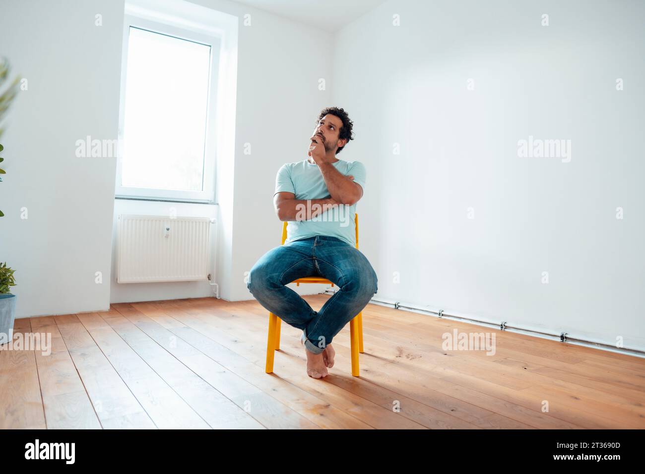 Contemplative man sitting on chair in front of wall at home Stock Photo