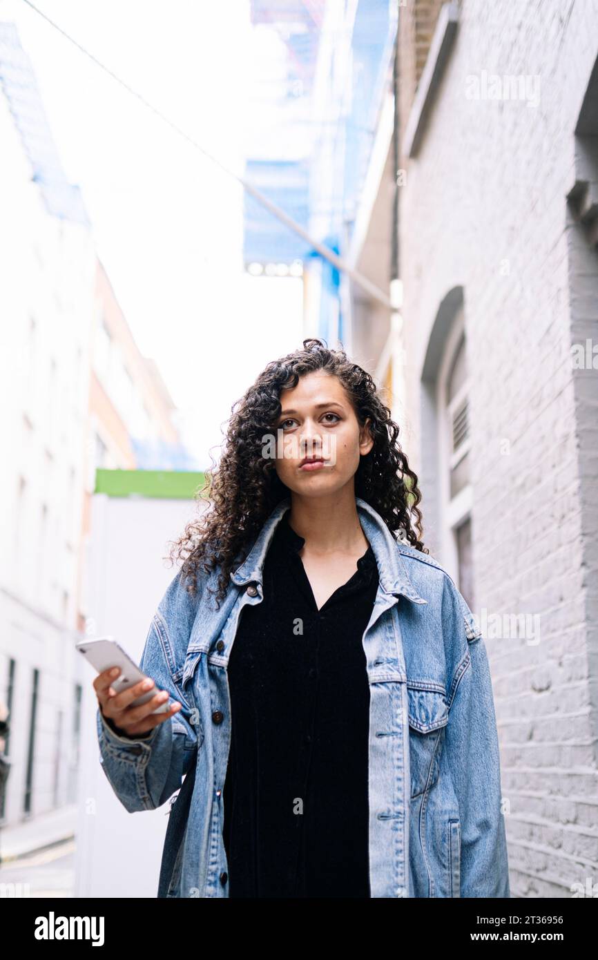 Contemplative young woman standing with smart phone Stock Photo