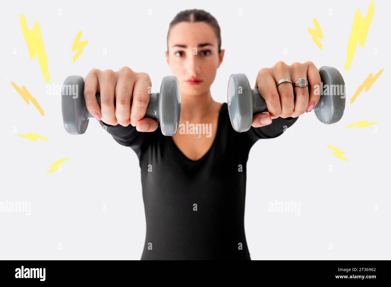 Woman exercising with dumbbell in front of white wall Stock Photo
