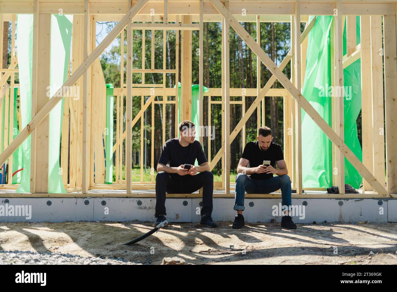 Engineers using smart phone sitting at construction site Stock Photo
