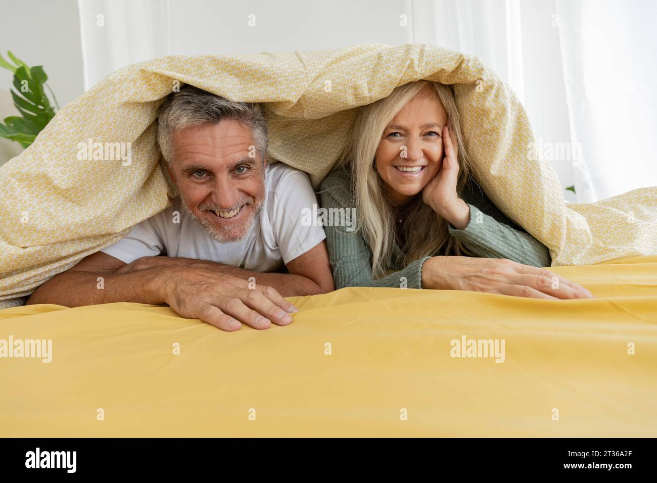 Happy mature couple lying under blanket on bed at home Stock Photo