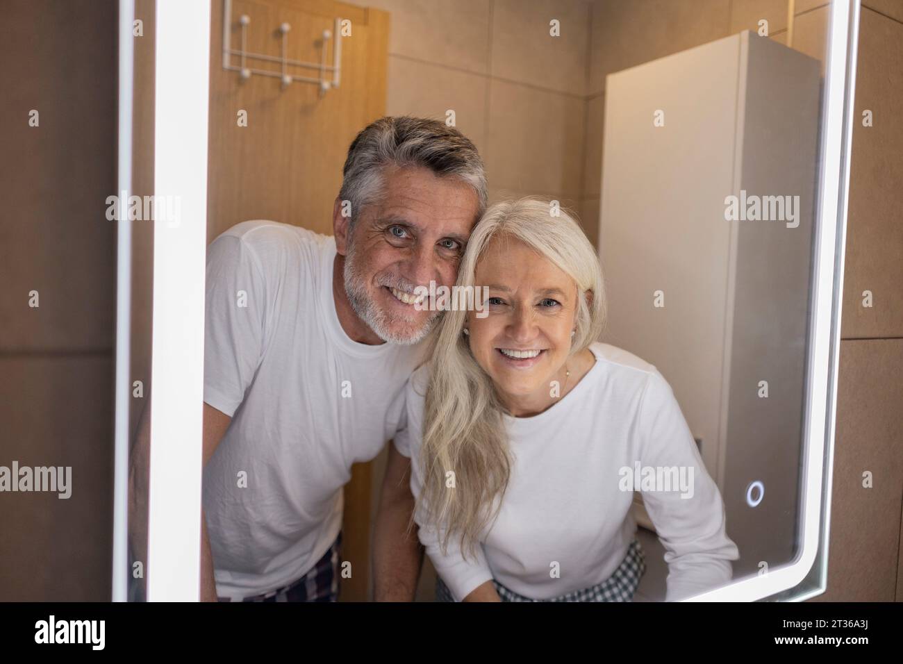 Reflection of happy man and woman in illuminated mirror at home Stock Photo