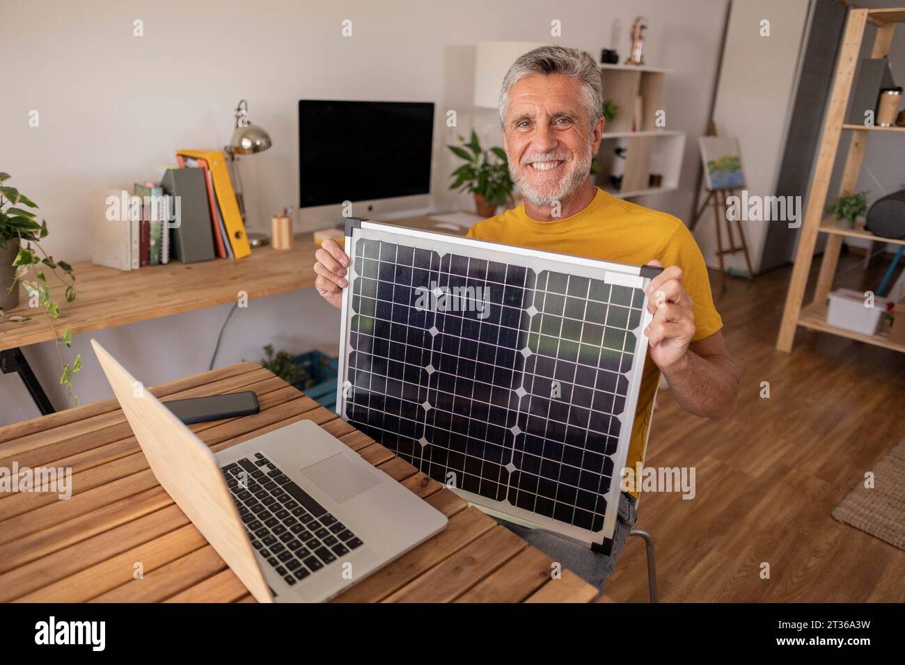 Happy engineer showing solar panel sitting with laptop on desk at home ...