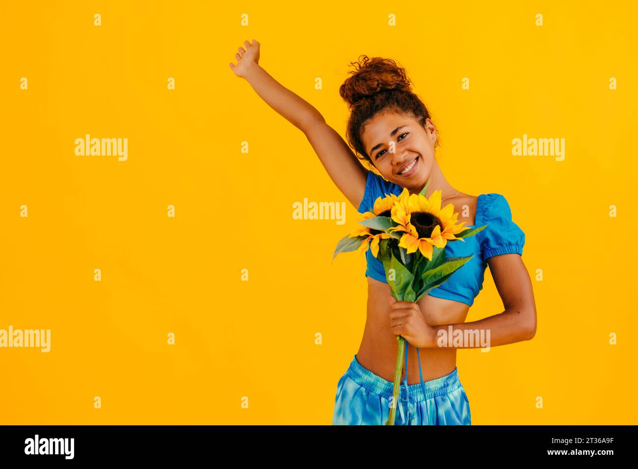 Happy woman with hand raised holding sunflower against yellow ...