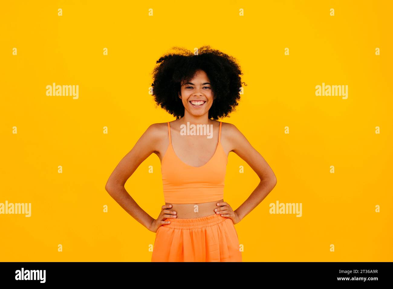 Happy woman standing with arms akimbo against yellow background Stock Photo