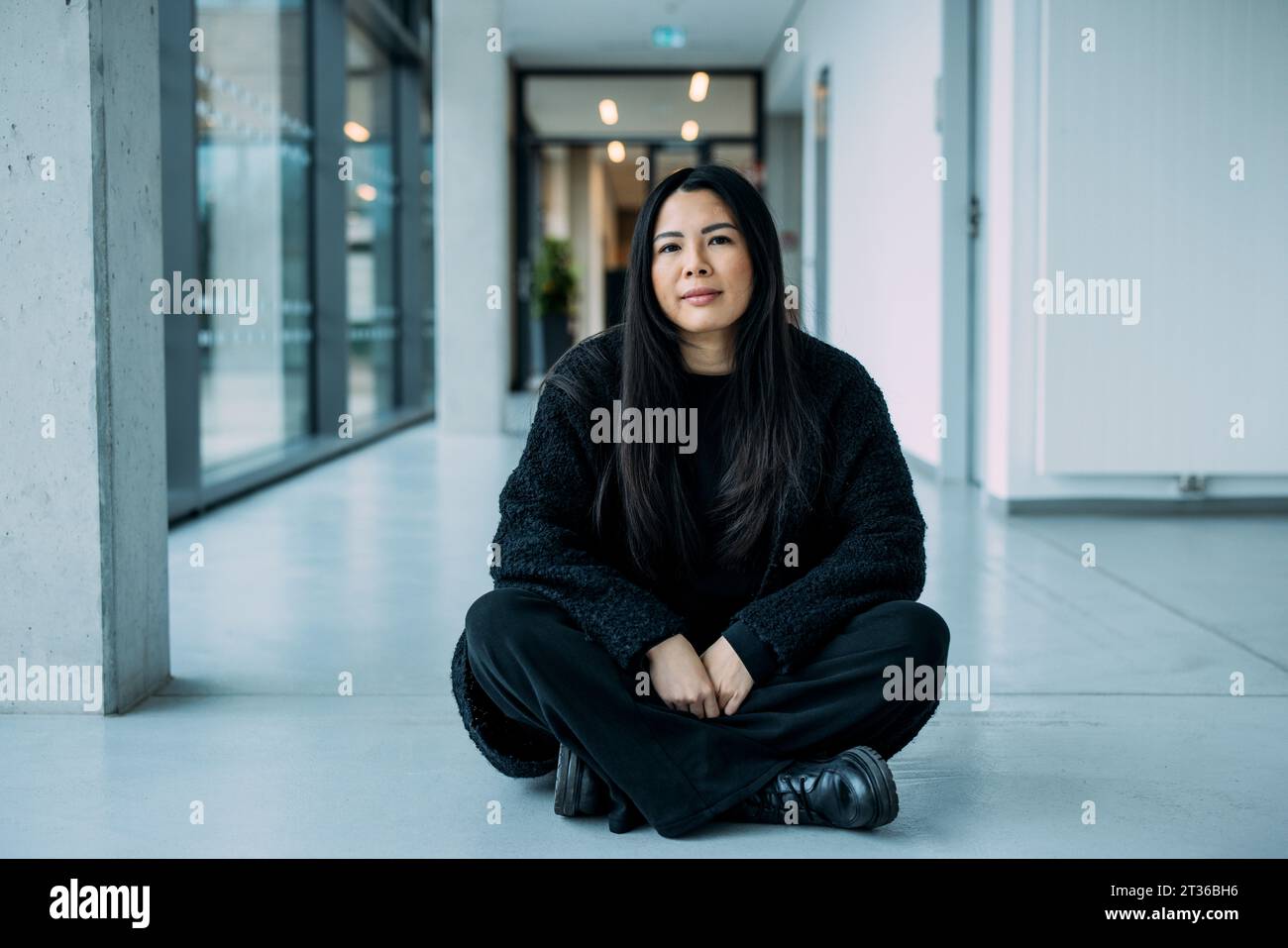 Businesswoman sitting cross-legged on floor in corridor at workplace Stock Photo