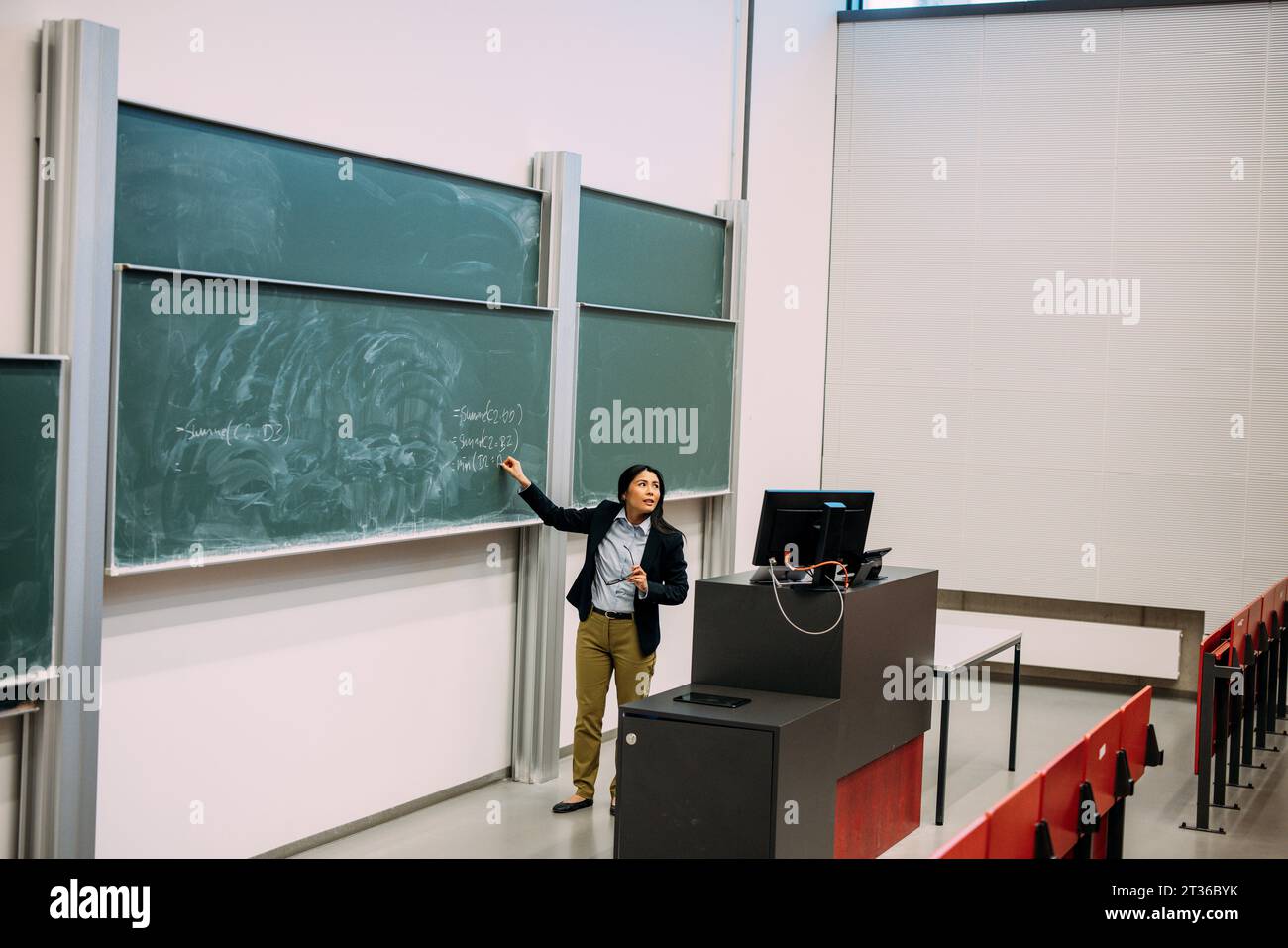 Confident businesswoman explaining strategy standing by greenboard at auditorium Stock Photo