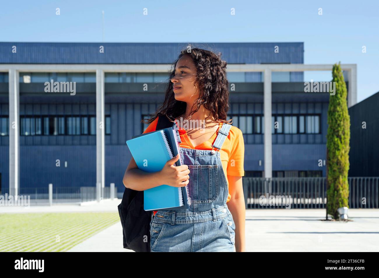 Student holding spiral notebooks and walking in front of building Stock Photo