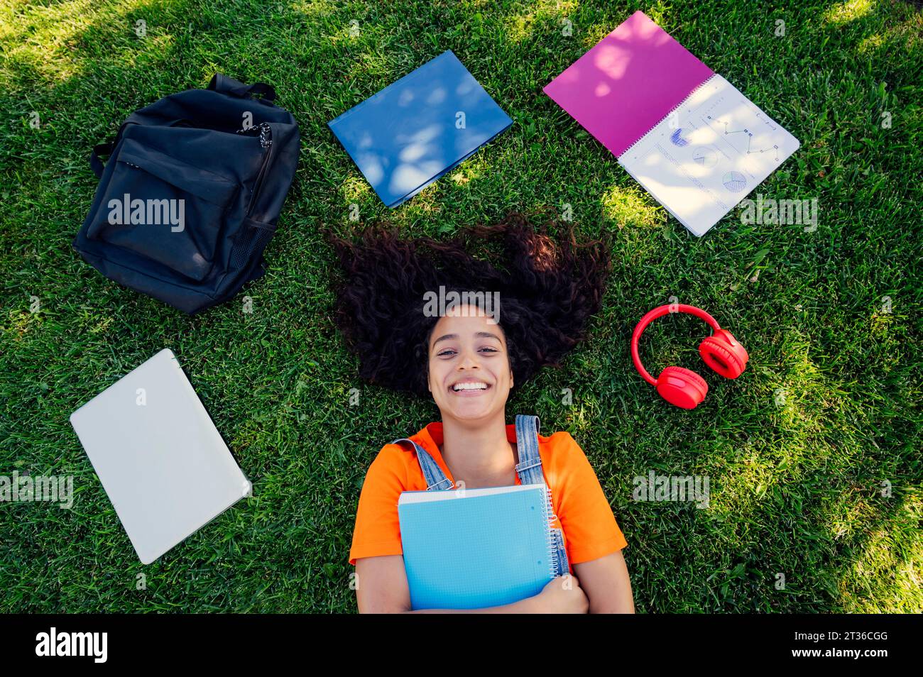 Smiling student lying on grass with spiral notebooks in campus Stock Photo
