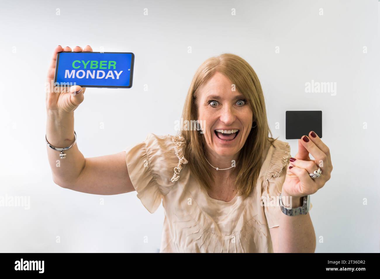 Crazy woman holding mobile phone with Cyber Monday advertisement on the screen and a credit card mock-up. Stock Photo