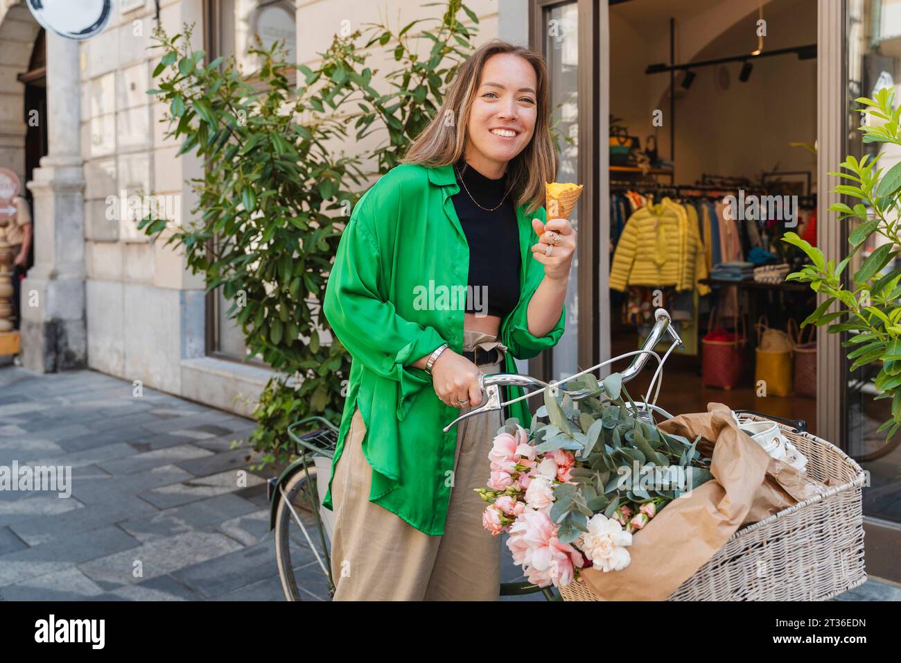 Smiling woman with bicycle having ice cream cone on footpath Stock Photo