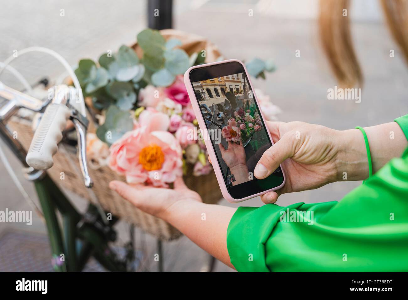 Woman taking picture of flowers in bicycle basket through smart phone Stock Photo