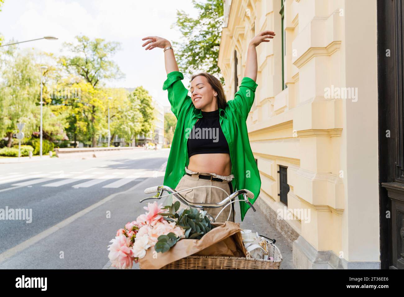 Happy woman with bicycle and arms raised on street Stock Photo