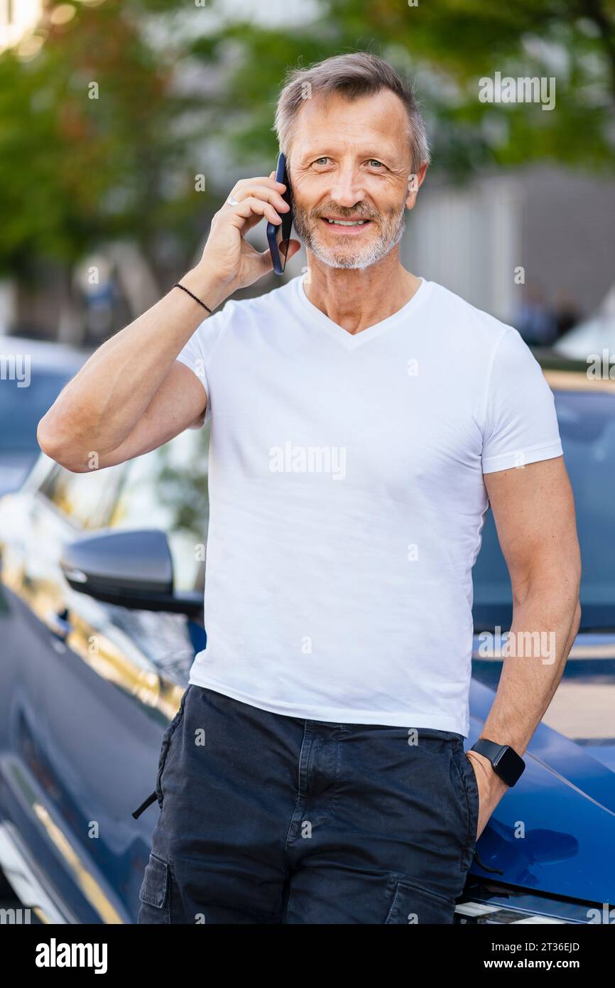 Smiling man talking over smart phone and leaning on car Stock Photo