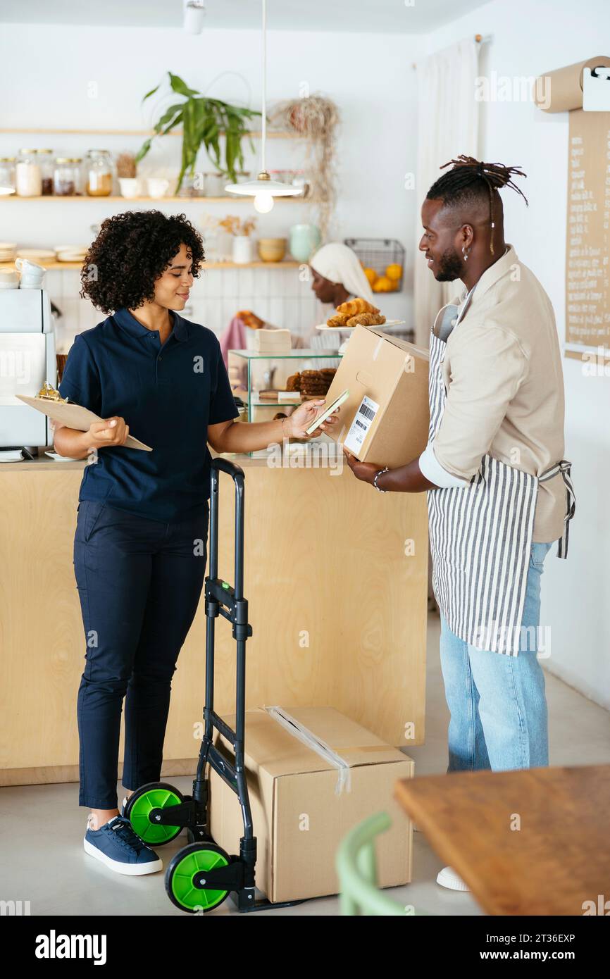 Smiling waiter holding package and delivery woman scanning QR code in