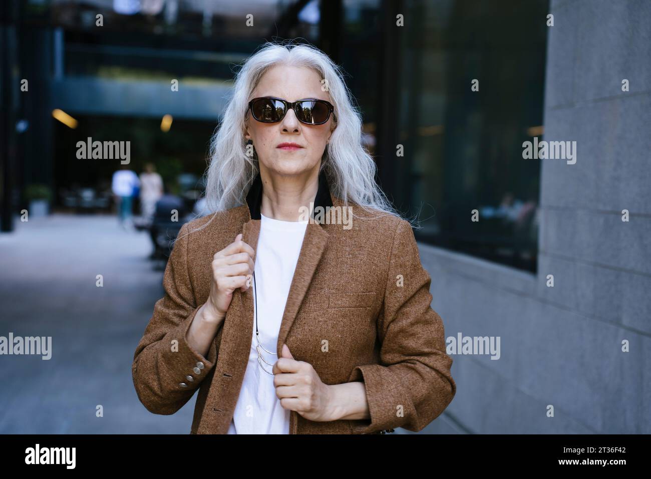 Mature businesswoman wearing brown jacket standing on street Stock Photo