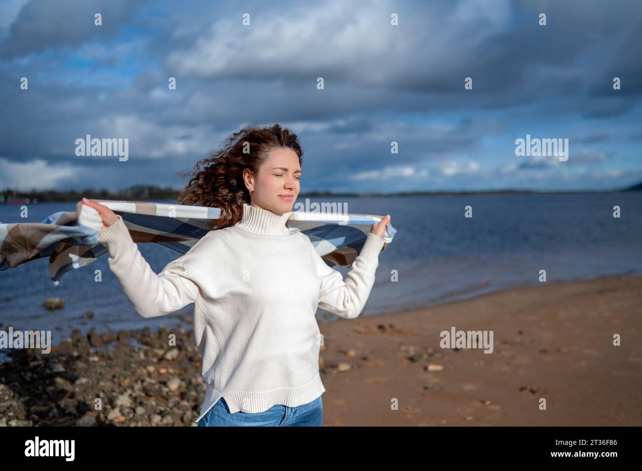 Smiling woman with eyes closed holding shawl at beach Stock Photo