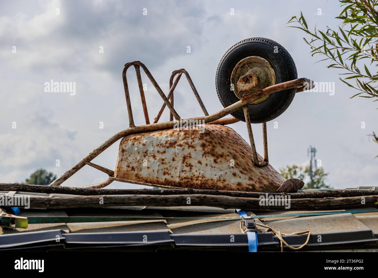 Old rusty white metal wheelbarrow upside down abandoned on wooden planks on deck of a ship against gray cloud covered sky in background, cloudy summer Stock Photo