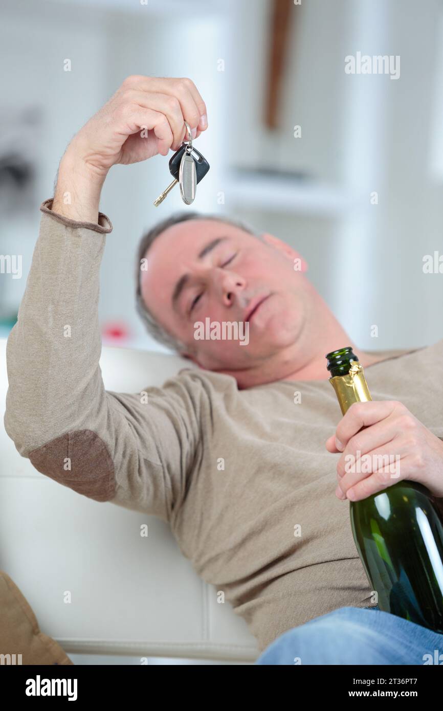 drunken man holding bottle of drink looking at car keys Stock Photo