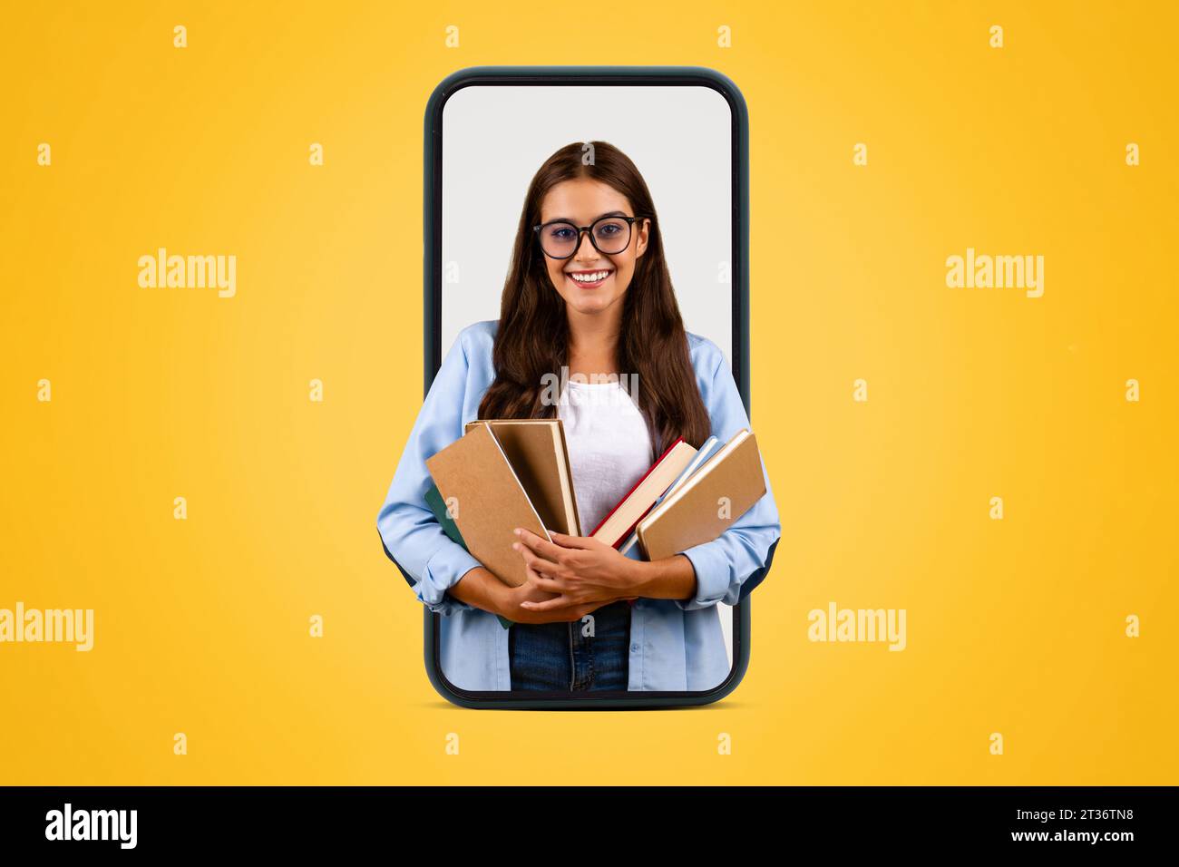 Smiling young student lady in glasses hold many books on big phone ...