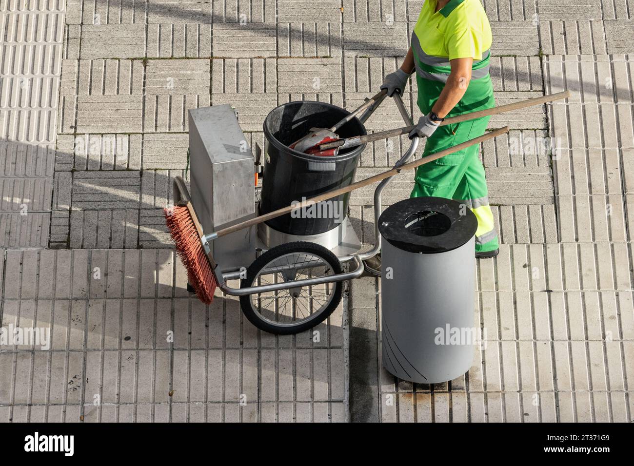 A sweeper worker pushing a cart on a city sidewalk. Urban cleaning