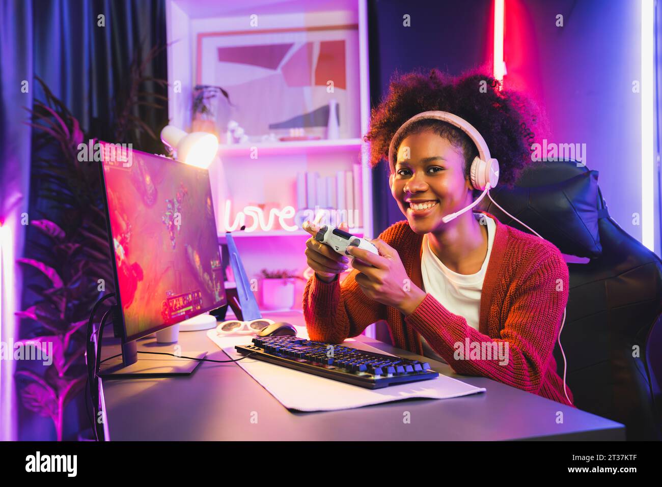 African American girl gaming streamer team winner playing online fighting with Esport wearing headphones in neon lighting room. Talking other players Stock Photo