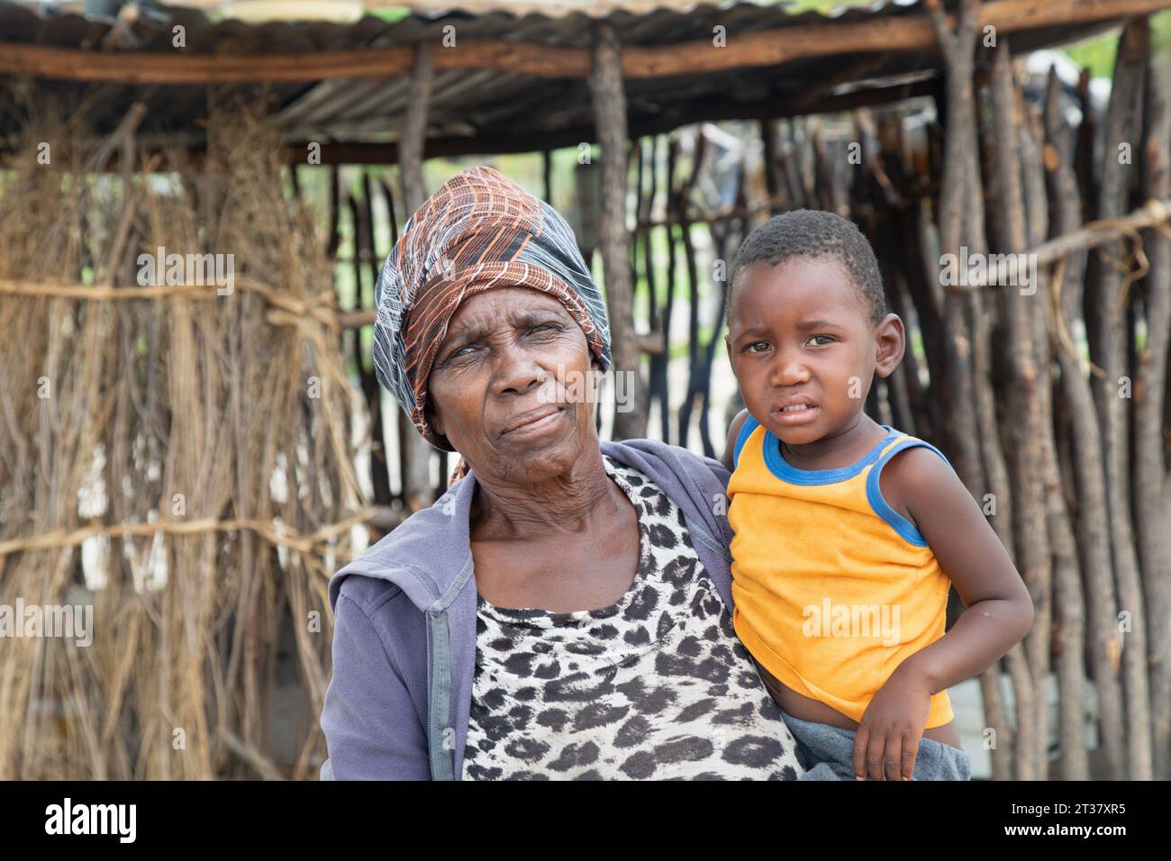 african village ,granny holding her grandchild in front of the outdoors kitchen in the yard Stock Photo