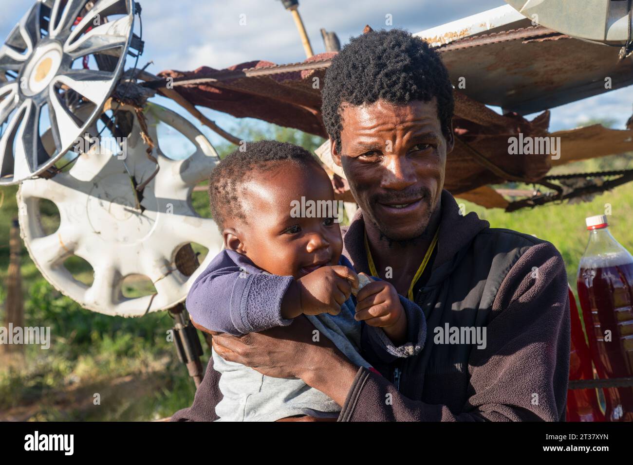 african village ,street vendor selling petrol gas in bottles by the side of the road, he is holding his baby. Stock Photo