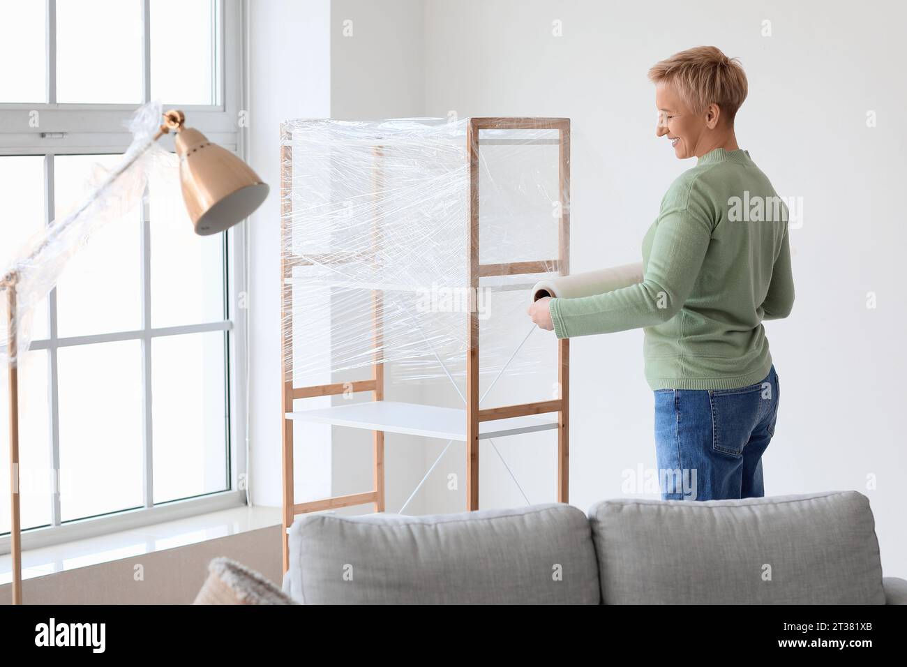 Mature woman wrapping shelving unit with stretch film at home Stock Photo