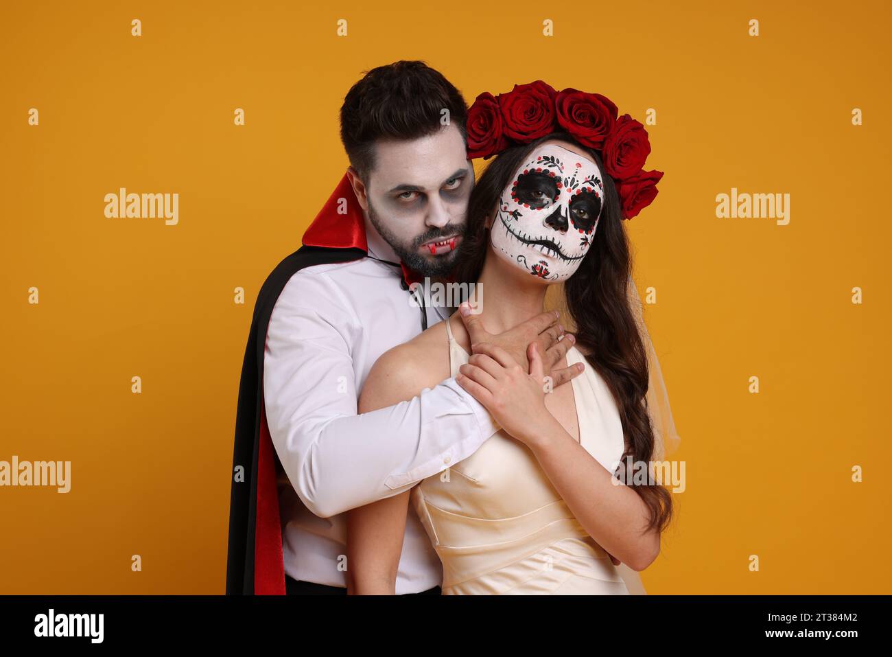 Couple in scary bride and vampire costumes on orange background. Halloween celebration Stock Photo