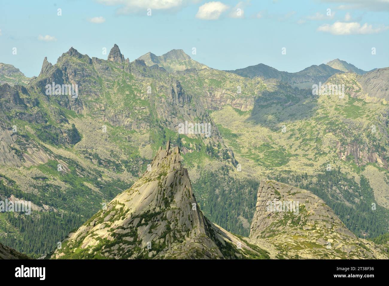 A large double-headed rock with steep slopes against the backdrop of pointed mountain peaks on a sunny summer day. Parabola Rock, Ergaki Nature Park, Stock Photo