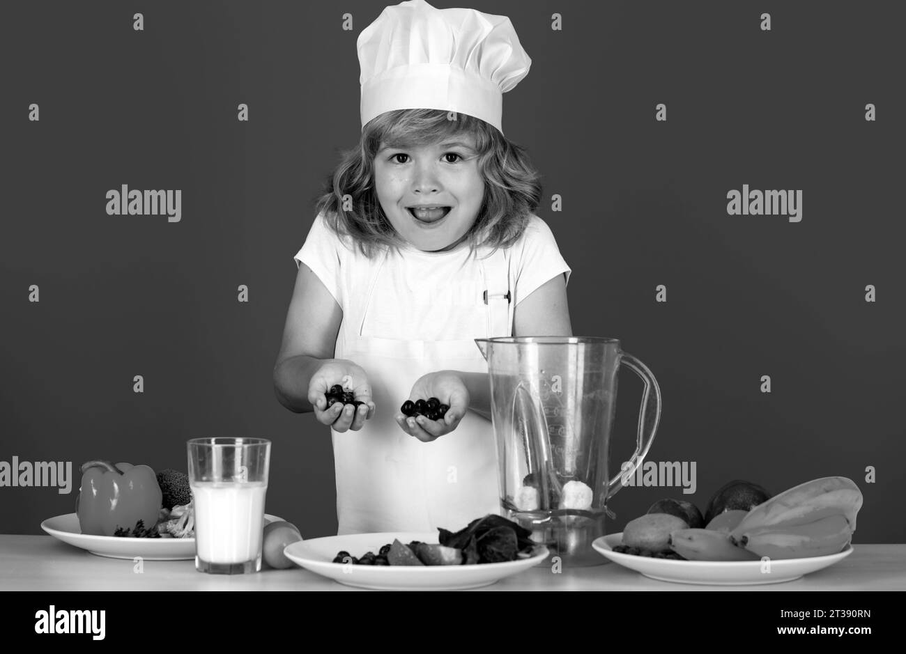 Excited funny chef cook. Child chef dressed cook baker apron and chef hat cooking blueberries smoothie isolated on studio background. Healthy Stock Photo