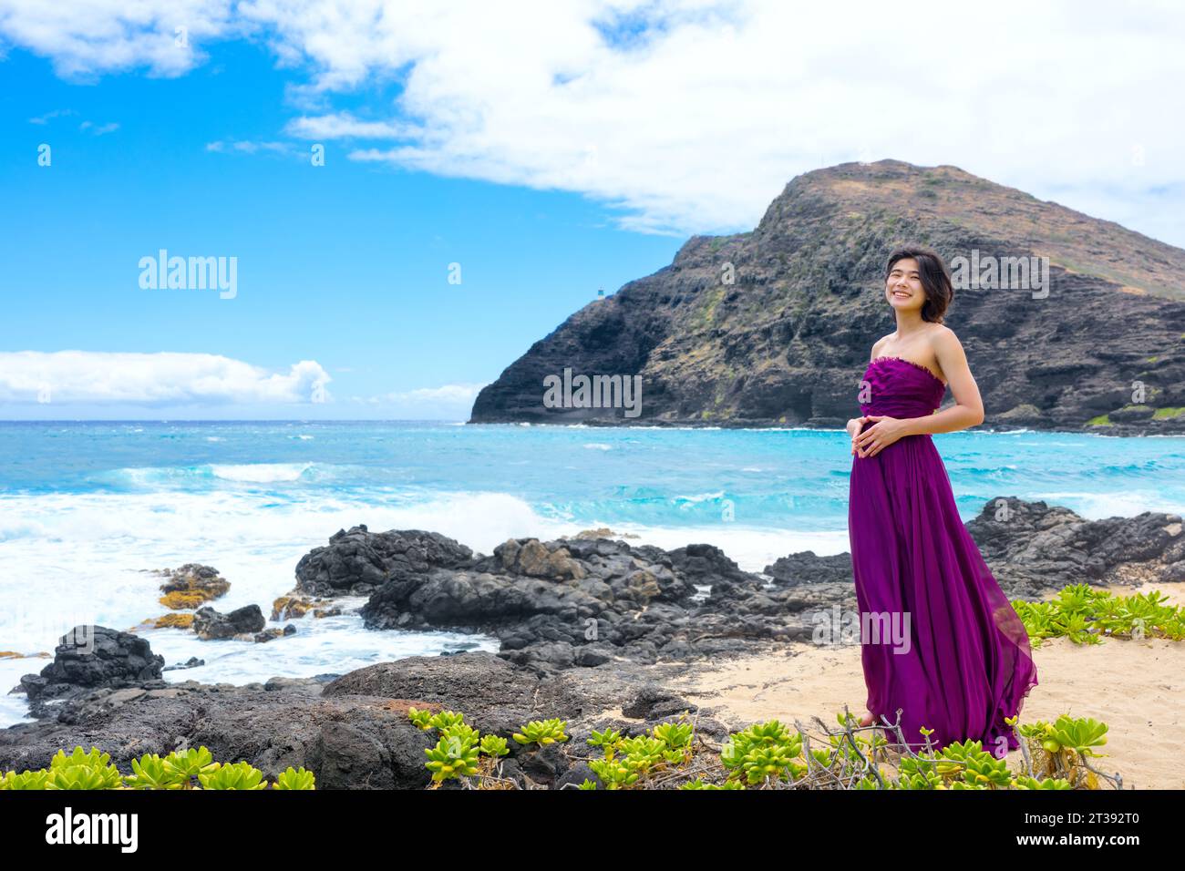 Teen girl in purple dress standing by rocky beach  on Hawaiian coast at Makapu'u beach Stock Photo