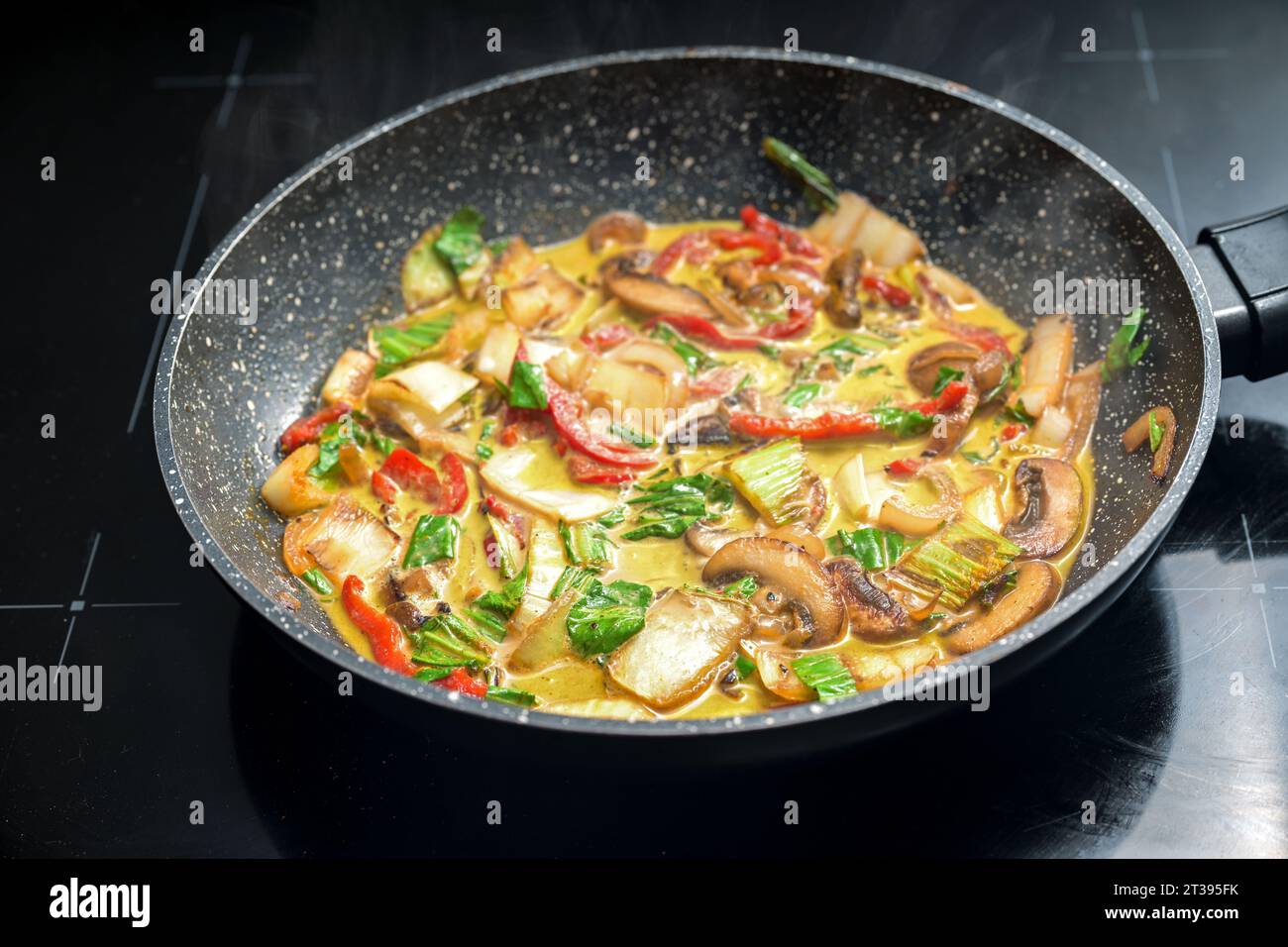 Vegetable Thai curry in a frying pan, ingredients like red bell pepper, mushroom, pak choi, seasoned with ginger, turmeric and onions, cooked in cocon Stock Photo
