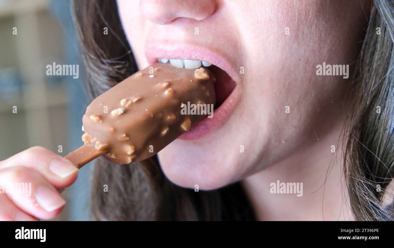 A young woman is indulging in a delectable chocolate covered treat, her mouth open wide in anticipation of the delicious flavor Stock Photo