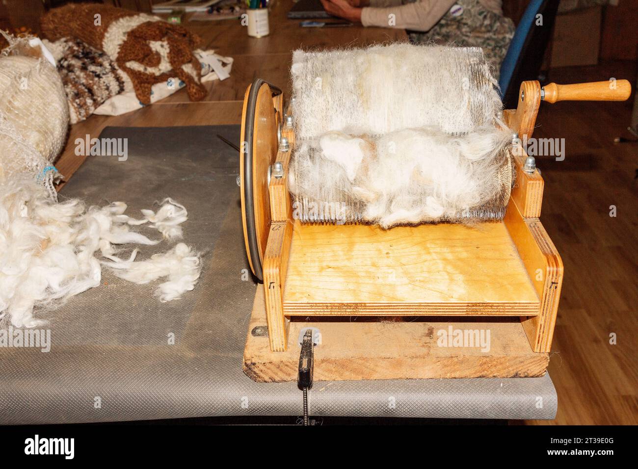 A handoperated wooden drum carder placed on a table with fluffy white