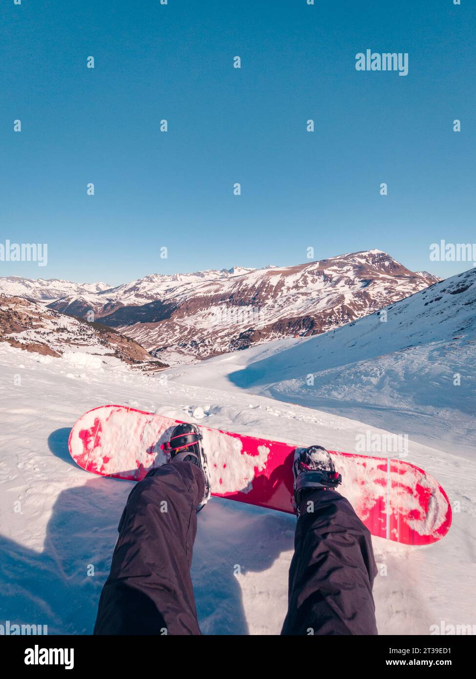 Cropped anonymous snowboarder in ski suit and with snowboard resting on snowy ground while spending winter vacation Stock Photo