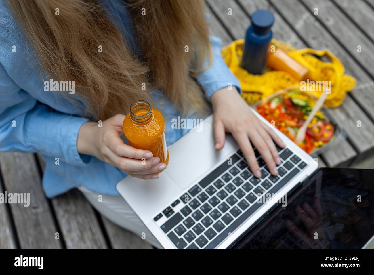 Top view of anonymous blond haired student with juice in her hand writing in notebook outside. Stock Photo