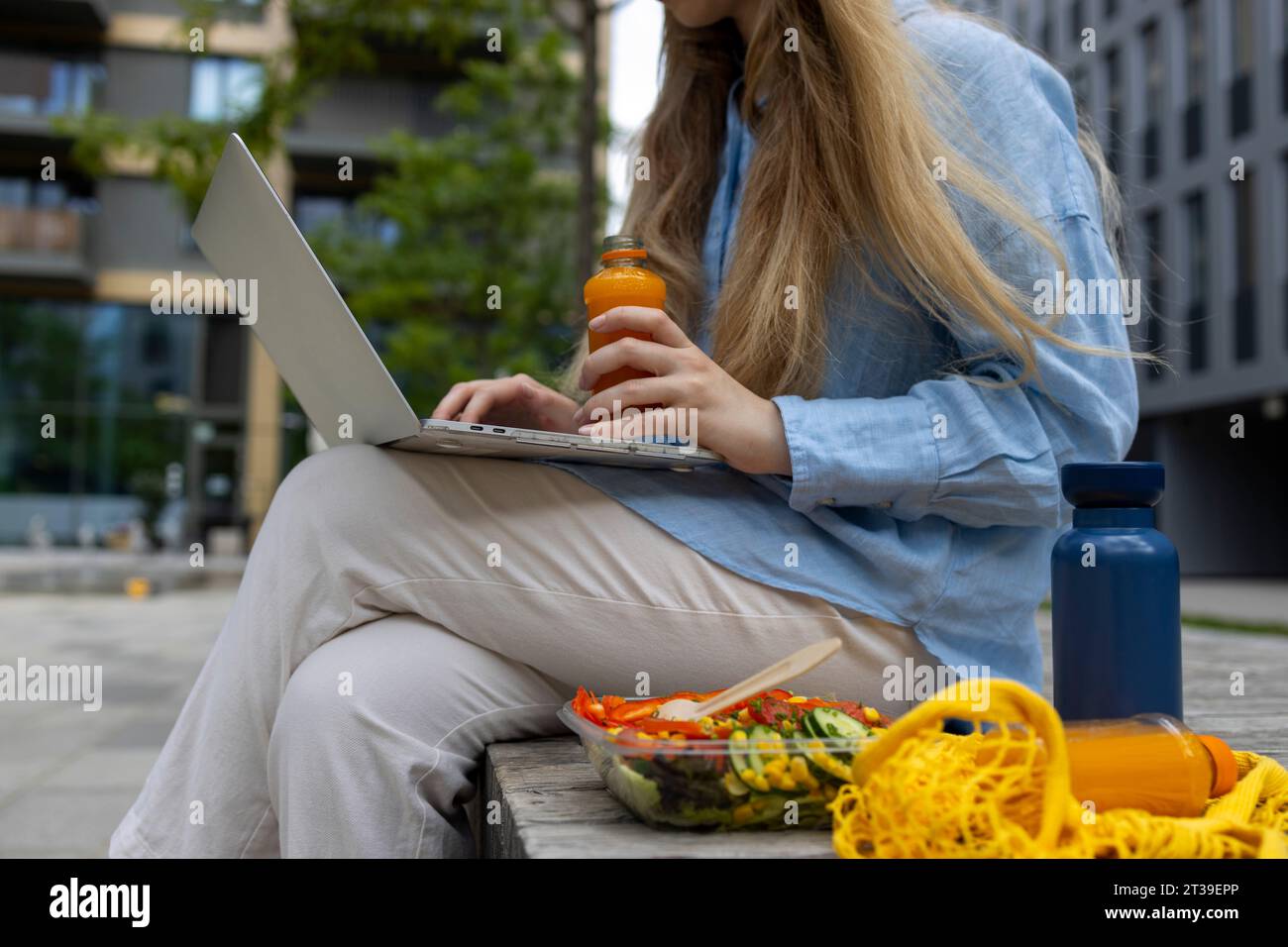 Anonymous blond haired student taking a break and writing in her laptop in an urban place. Low-angle view. Stock Photo
