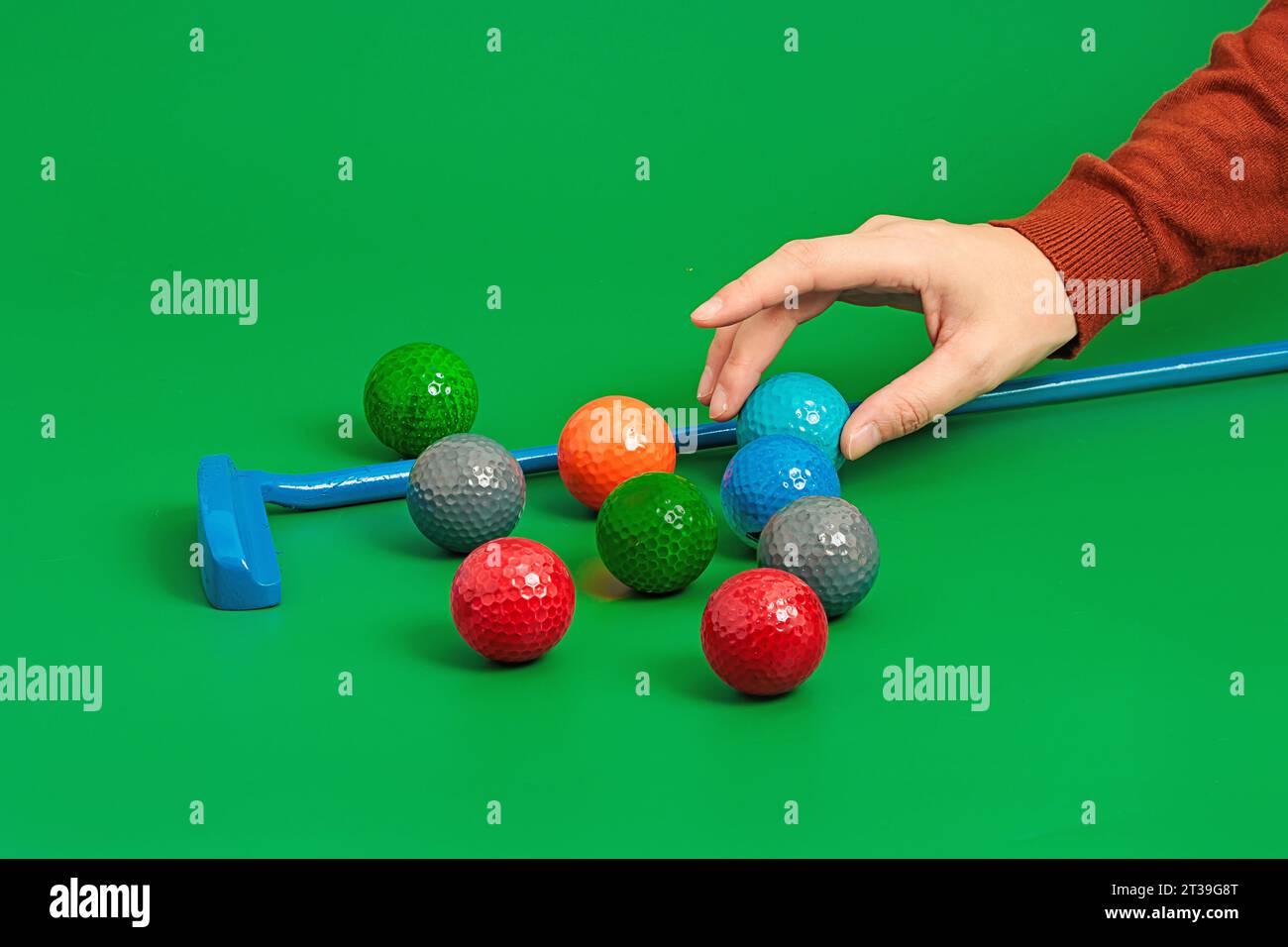 Crop hand putting ball into mini golf set on green surface in studio with golf stick and with various balls Stock Photo