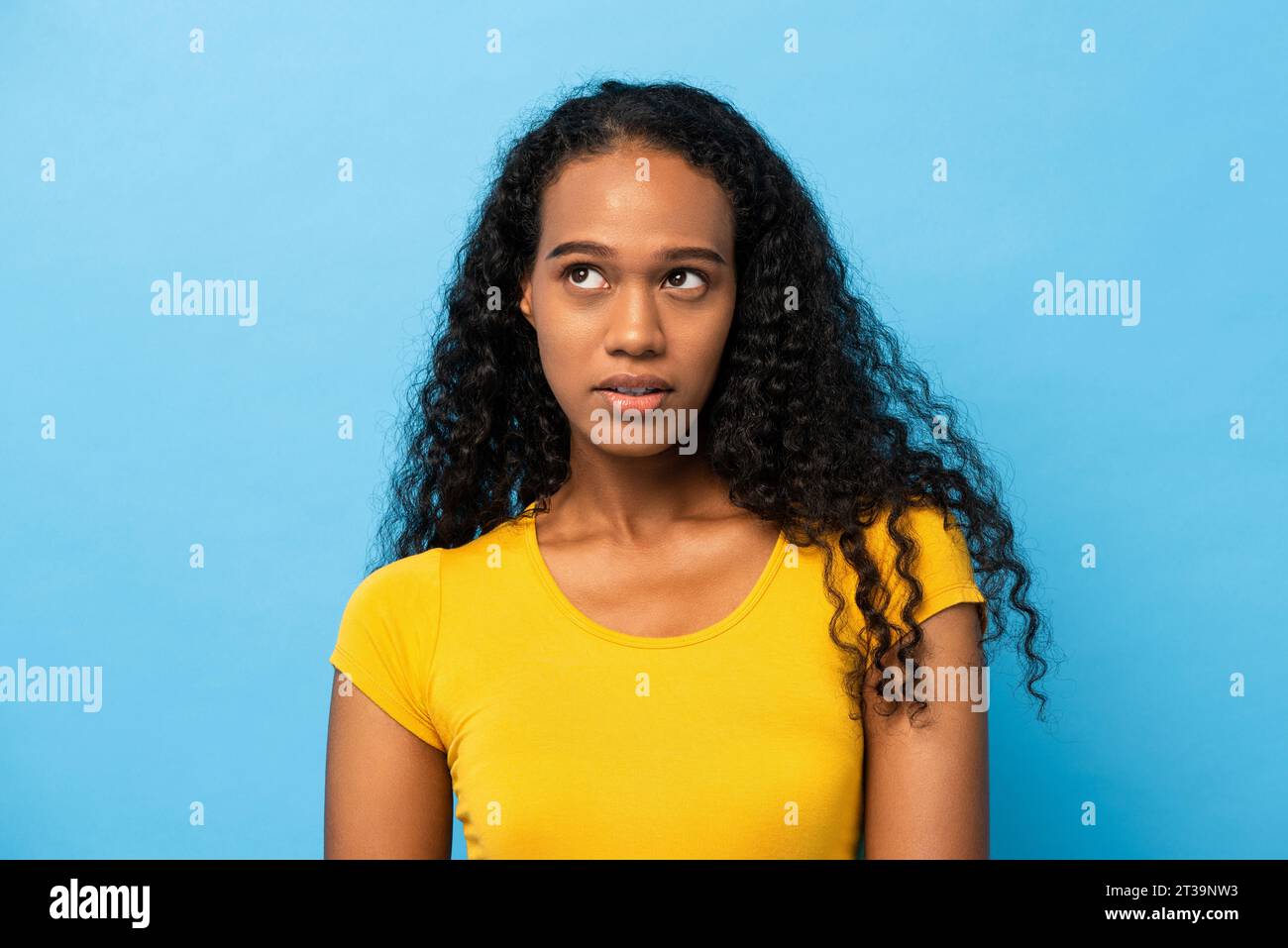 Portrait of mixed race African woman thinking with eyes looking up in light blue studio isolated background Stock Photo