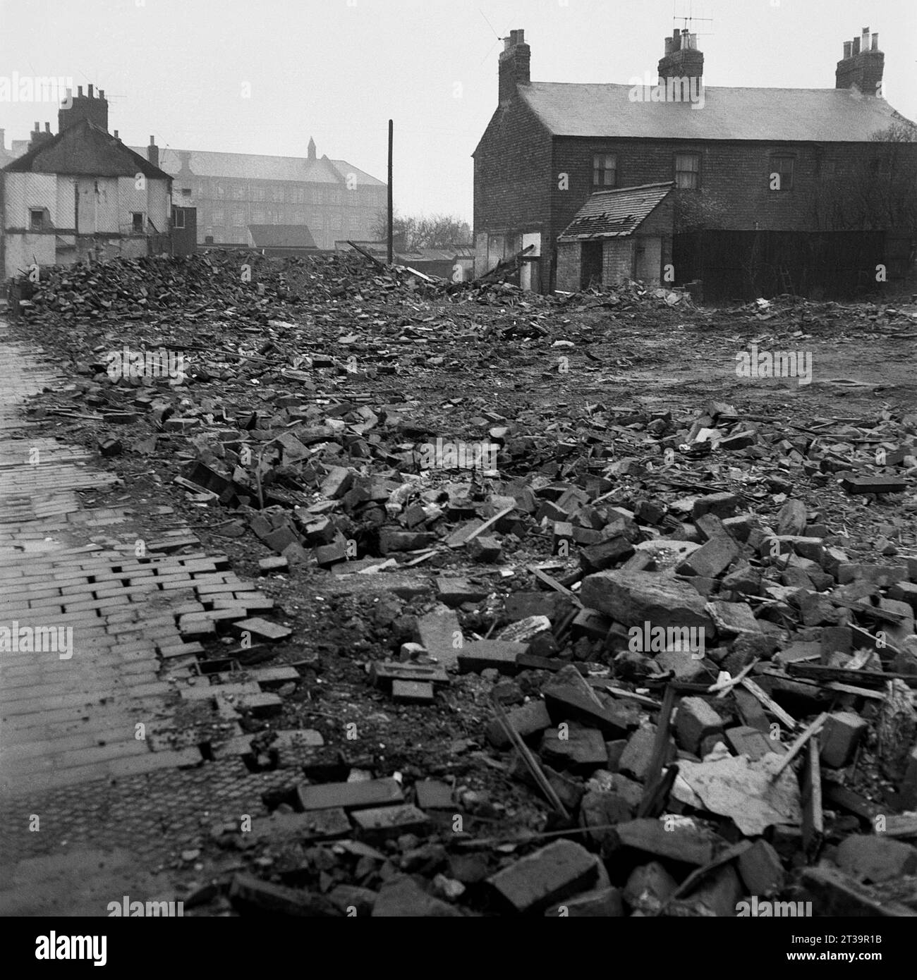 Rubble strewn wasteland with part demolished houses and a large factory